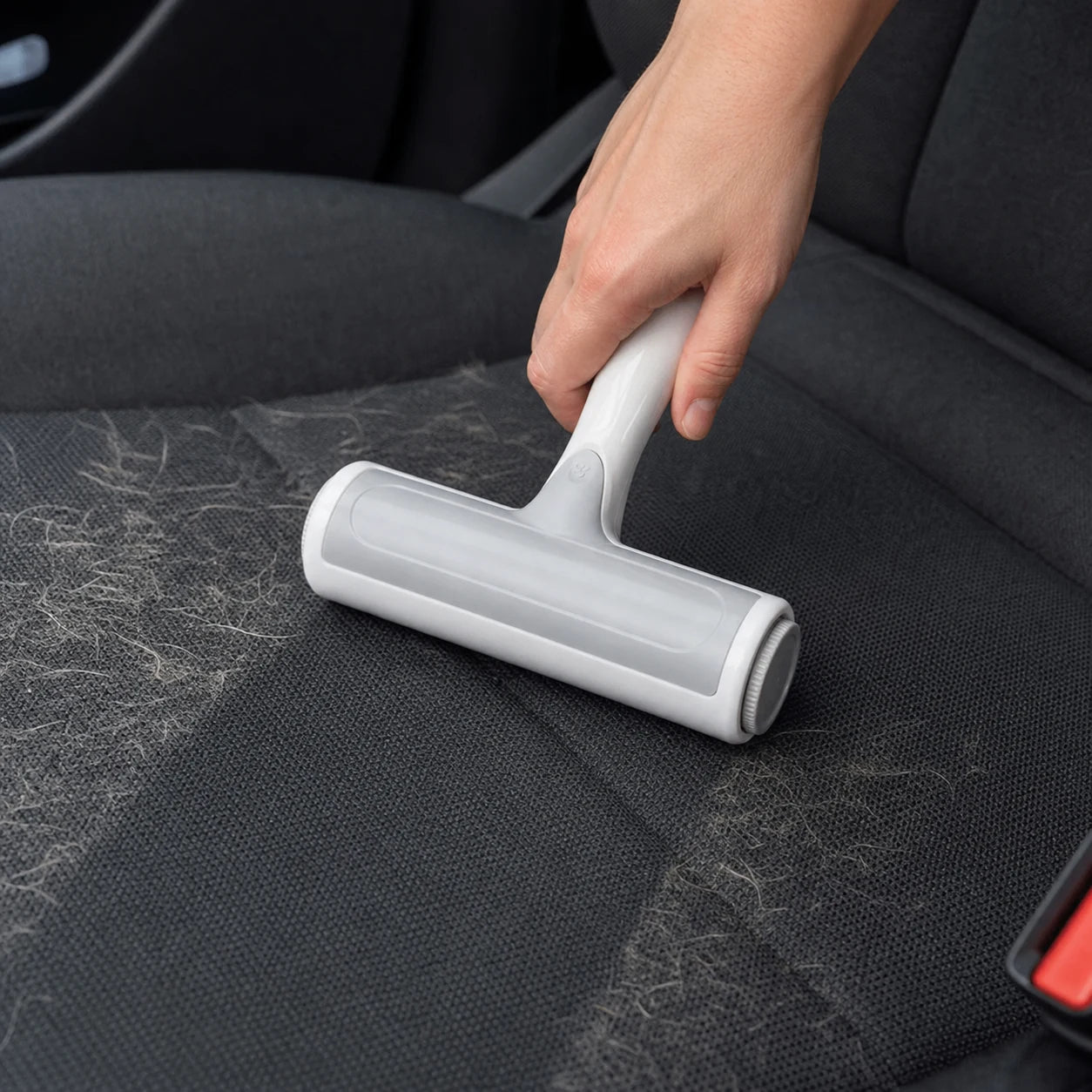 Gray reusable pet hair roller being used on a fabric car seat